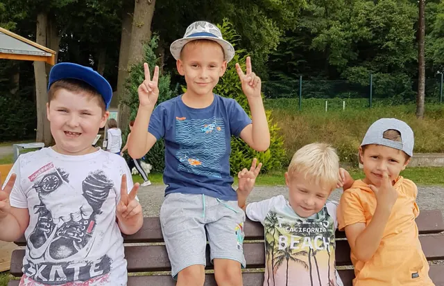 Vier fröhliche Vorschulkinder sitzen auf einer Bank im Freien